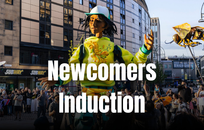 A giant puppet of a young black girl wearing a bright yellow hoodie walks through a crowd of people. Text reads 'Newcomers Induction'.